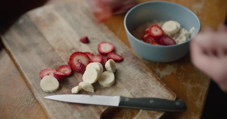 A person making breakfast with sliced strawberries and bananas