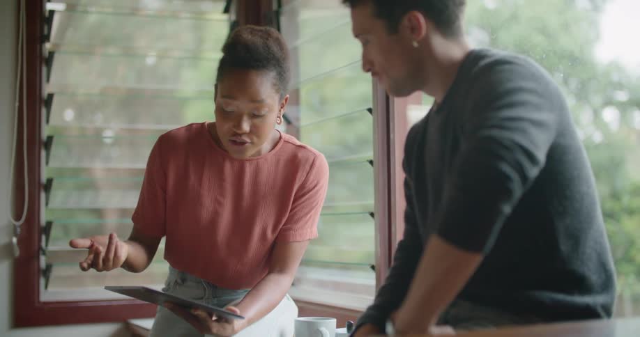 Young couple talking on the kitchen looking at a tablet in the morning