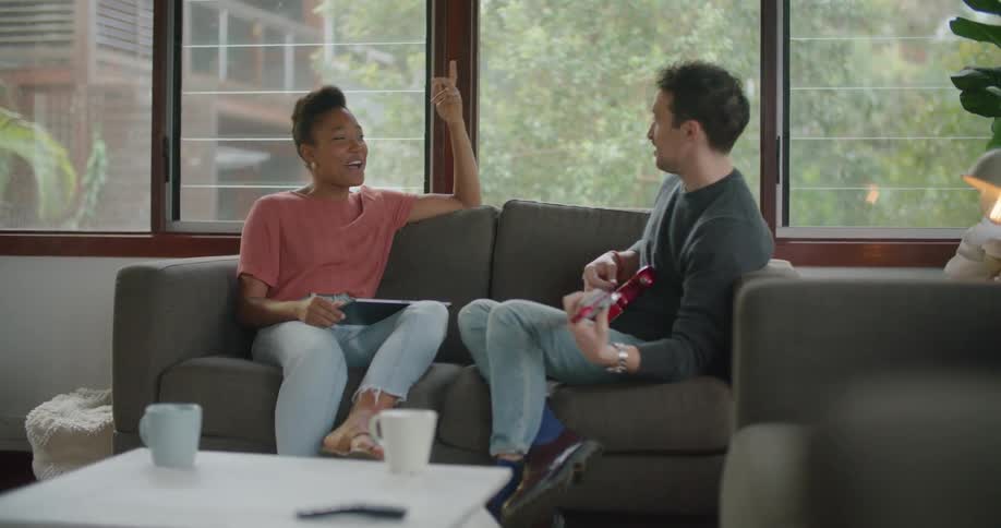 Man sitting on a couch playing a red guitar to a friend