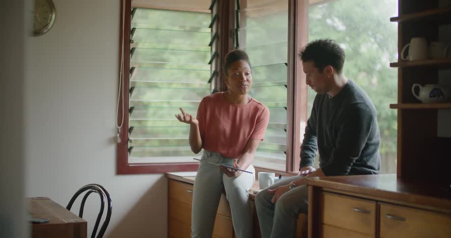 A woman and man sit beside a window talking about the tablet in the womans hand
