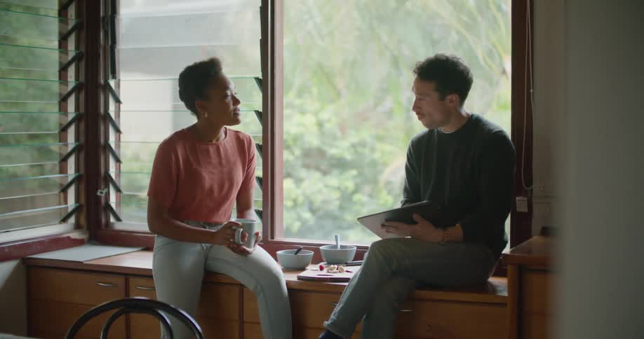 Woman drinks coffee sitting near window with man using tablet