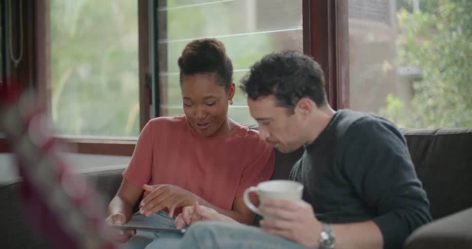 Man and woman sit near each other on couch sharing tablet