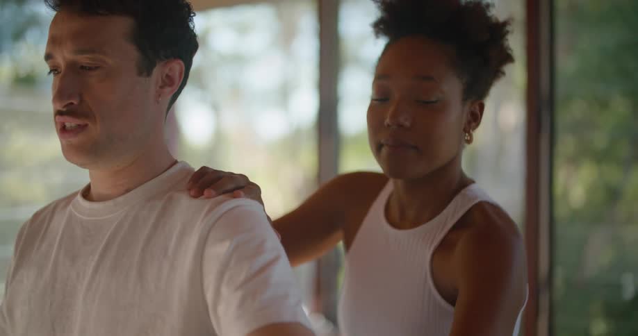 Woman helps man move shoulder through rotating stretching motion as he grimaces
