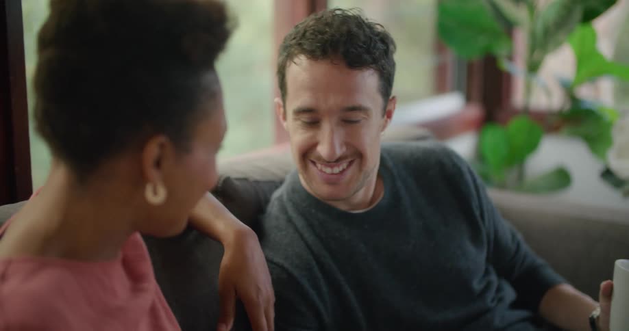 A man and woman sit on a couch and talk and look at a tablet