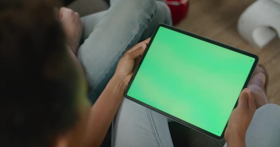 A woman sitting next to a man holds a tablet with a solid green screen