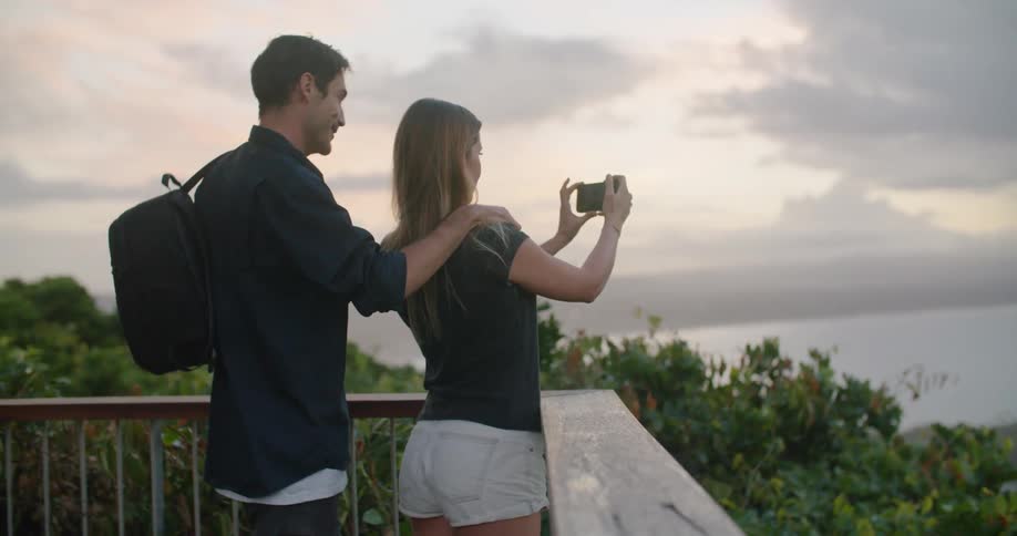 A man and woman stand on a balcony and take photos of the lake in front of them