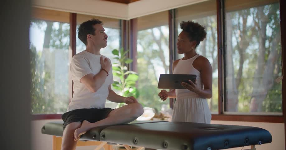 Man consults with massage therapist using tablet about his shoulder while sitting on massage table