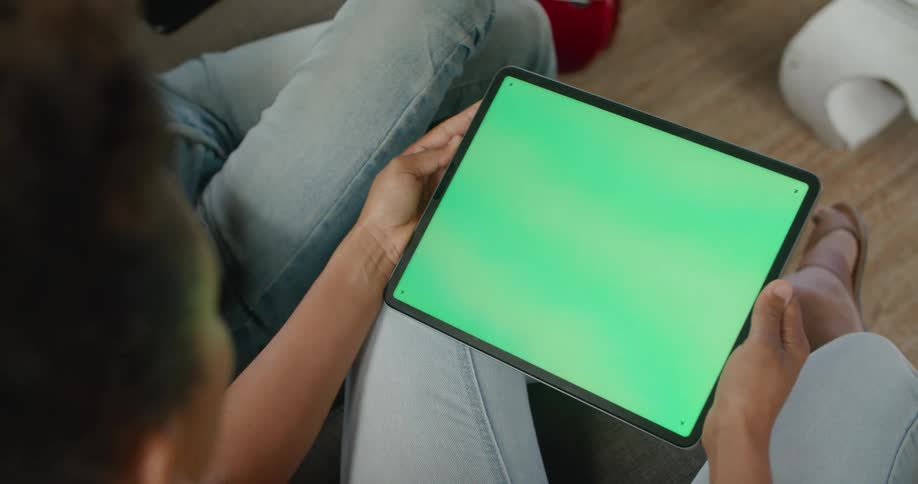 Man and woman sitting on couch hold tablet with green screen