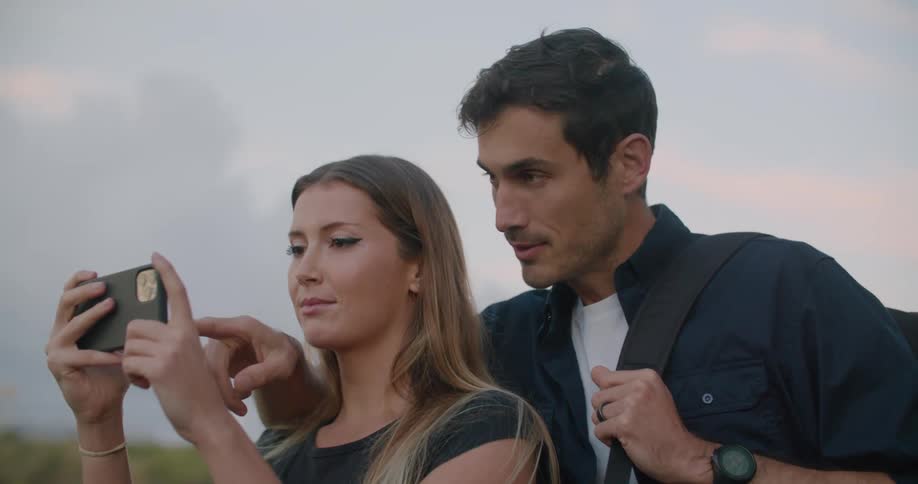 Man stands close to woman with hand on her shoulder as she takes picture with mobile phone