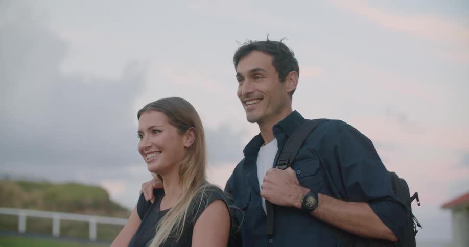 A man and woman walk over to a large farm style fence and look to the scenery