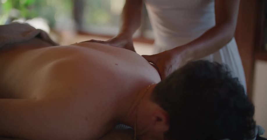 A massage therapist works on a mans back as he lies face down on a table