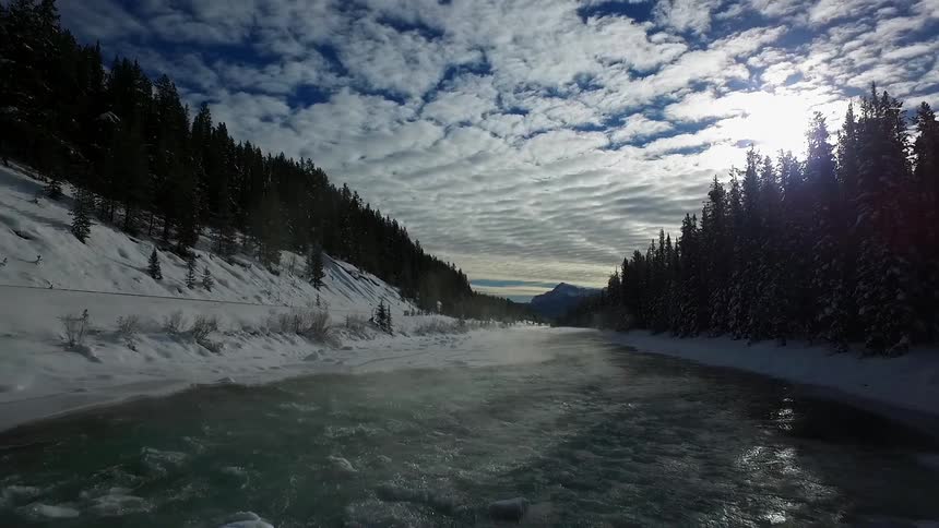 Aerial view moving down a river with snowy treed banks on each side
