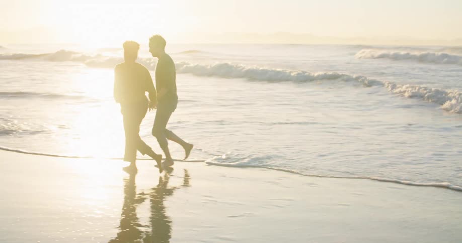 Man and woman hold hands and enjoy themselves next to sea at sunset
