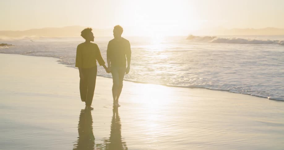 Silhouette of a young couple holding hands walking on a beach at sunset