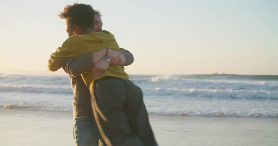 A man hugs a woman and swings her around on the beach