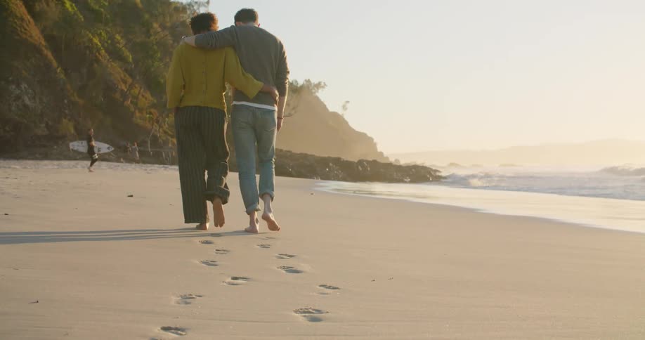 Two people walk close together on the beach then move quickly from the incoming wave
