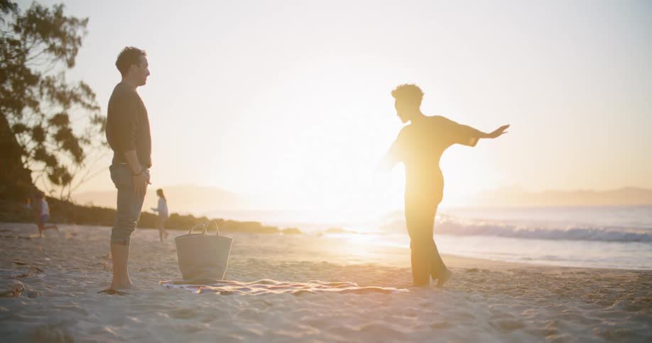 A man and woman lay a blanket down on the beach together
