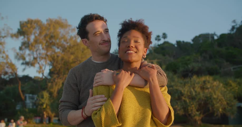 A man and woman hug in a park as they look at the fall trees