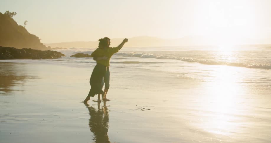 A man and a woman dancing on a beach with the ocean the sky and clouds in the background