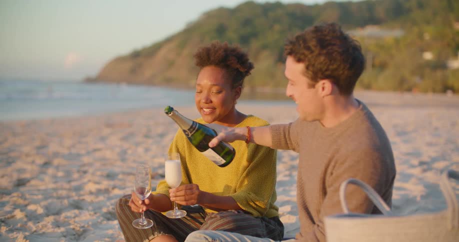 A man and woman sitting outside on the beach drinking wine