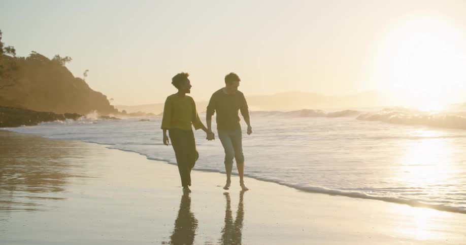 A couple hold hands while walking on the beach and run as ocean tide comes toward them