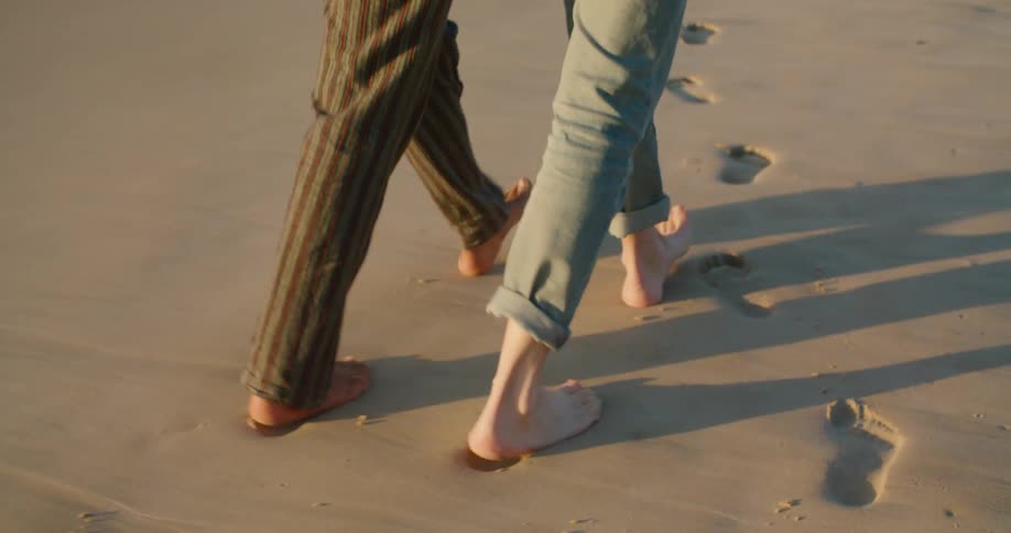 Two people walking on a sandy beach and leaving footprints