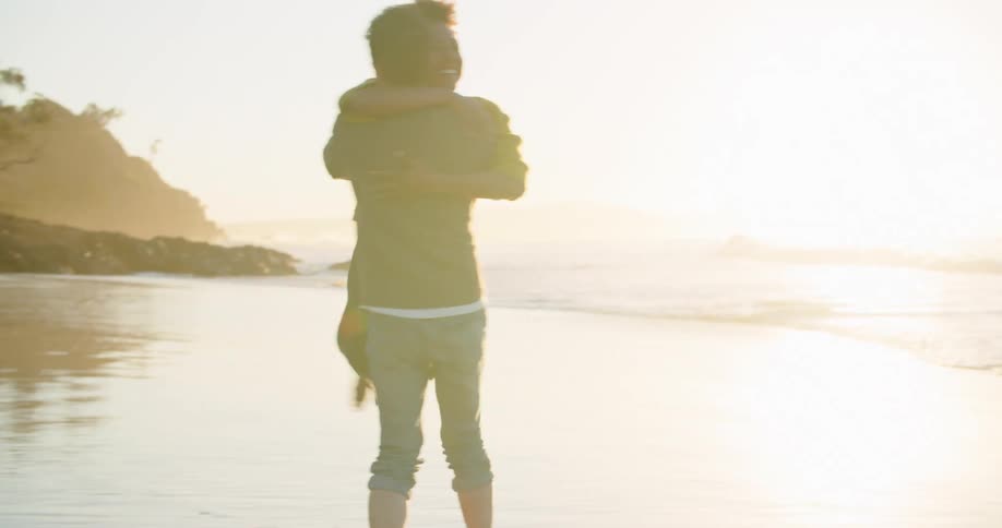 A man and a woman dancing on a beach with the ocean the sky and clouds in the background