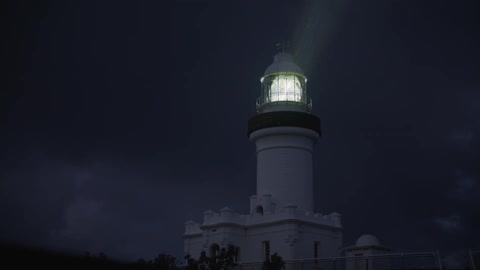 Light rotates in tower of lighthouse under cloudy sky at night