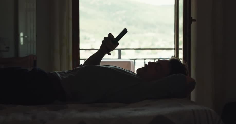 A man is laying on a bed and looking at a cell phone