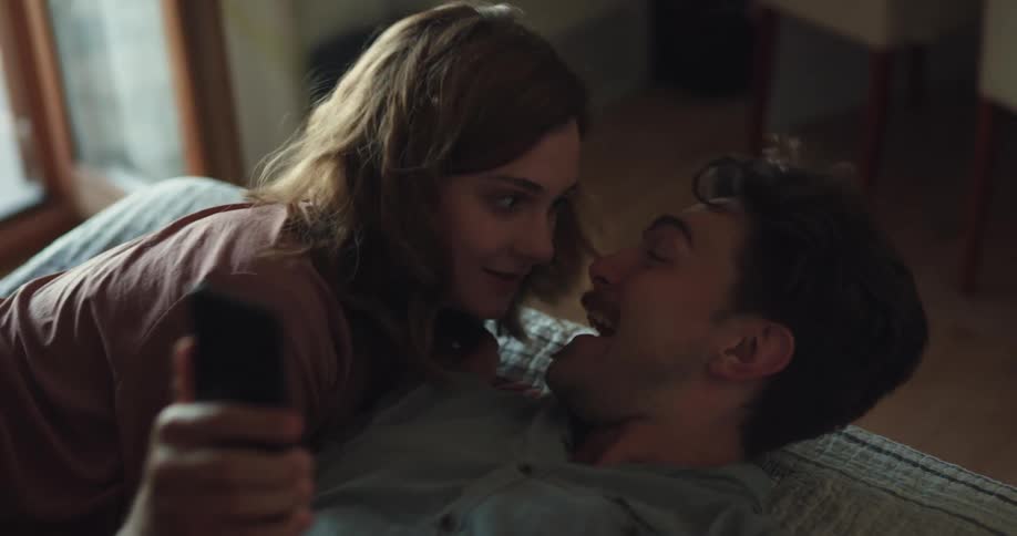 A man cheers as he looks at his cell phone and a woman lays next to him