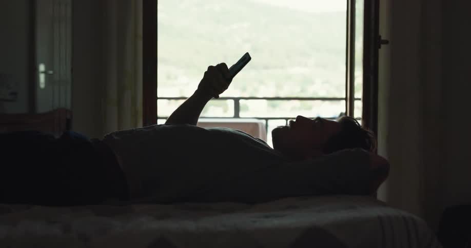 A man is laying on a bed next to a window