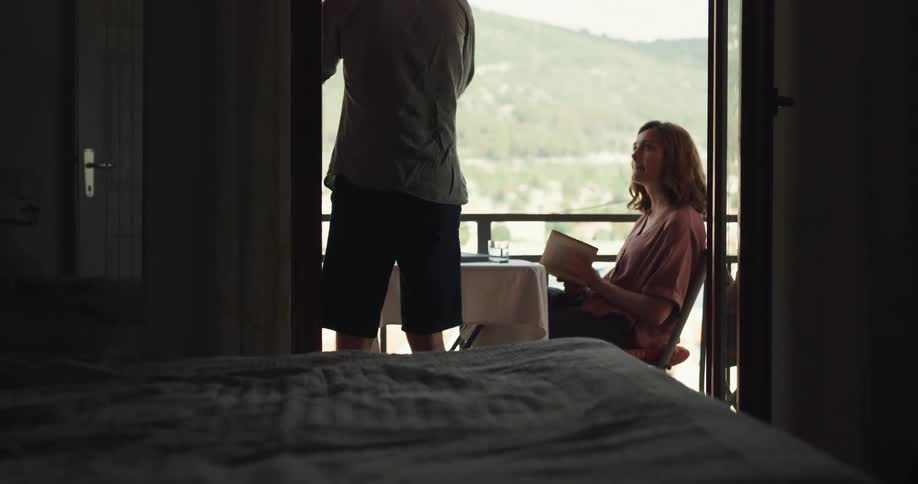 Man laying in bed drops cell phone and joins woman reading a book on balcony