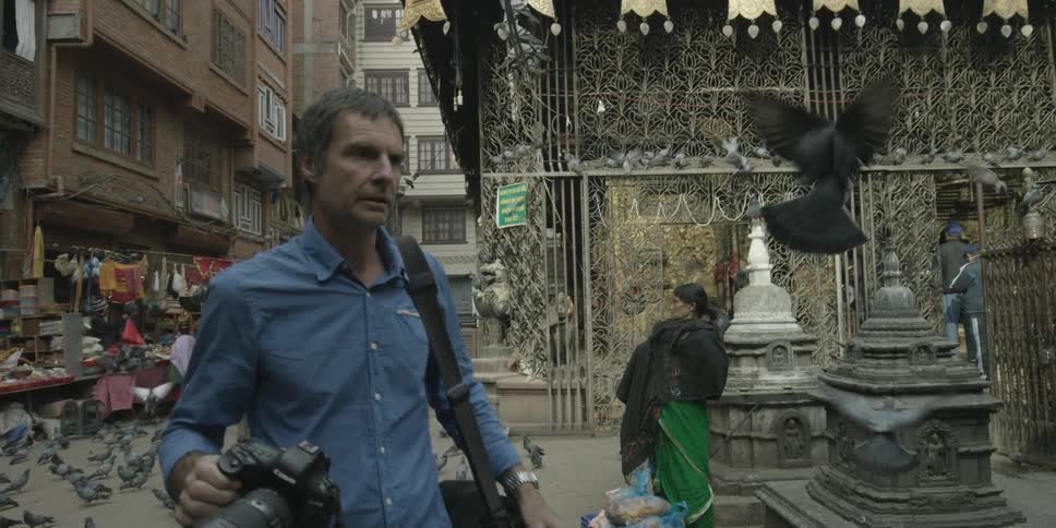 A man with a camera walks through an open marketplace in an asian country