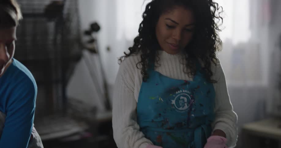 Two women in a room with aprons and gloves removing a sheet from a table