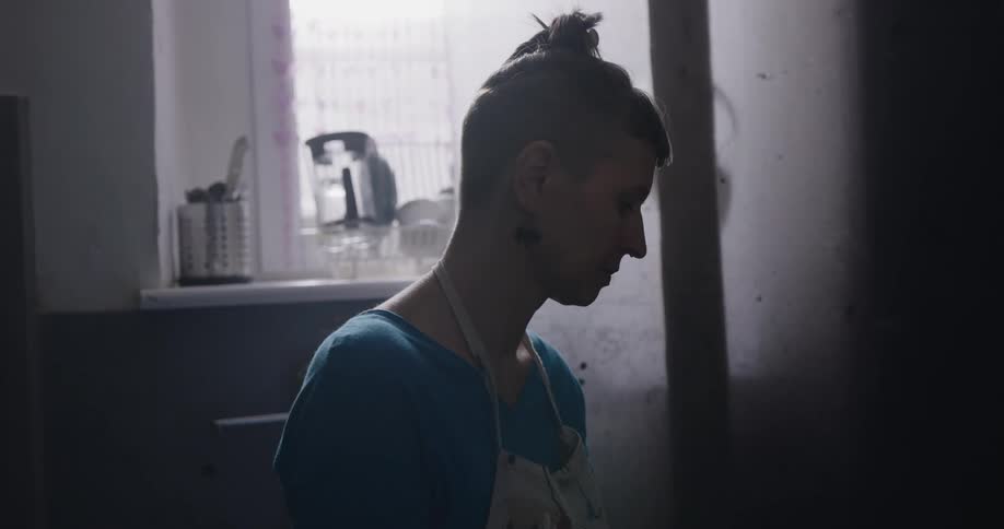 Woman wearing ink stained apron and gloves works in dimly lit room