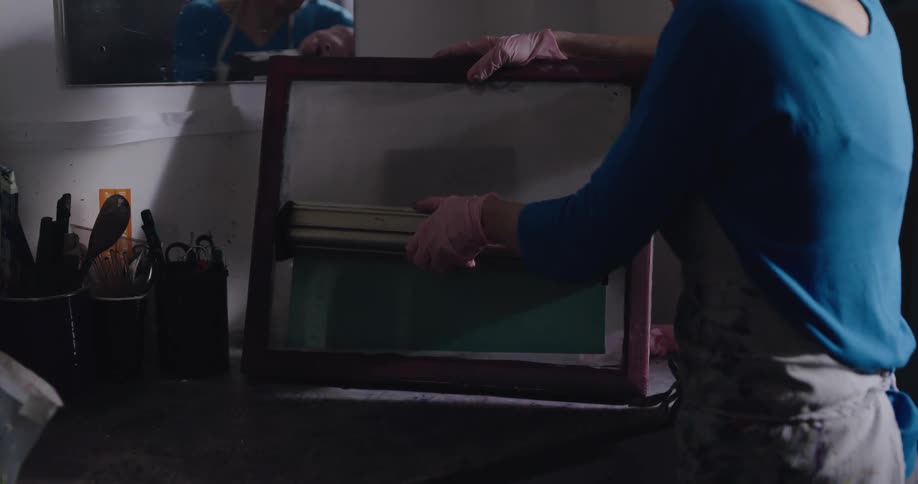 Female crafter works with silkscreen standing next to mirror