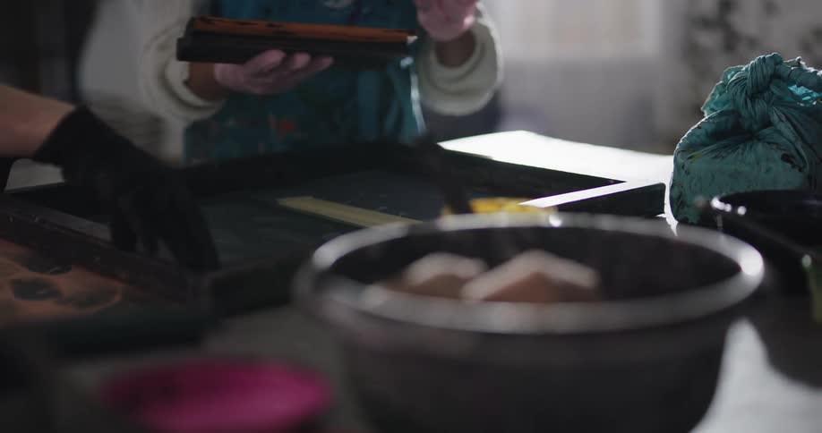 A man adds paint and dye onto fabric in a tray and a woman scrapes it through