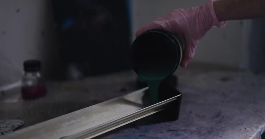 A person with gloves in a room pouring paint in a trough