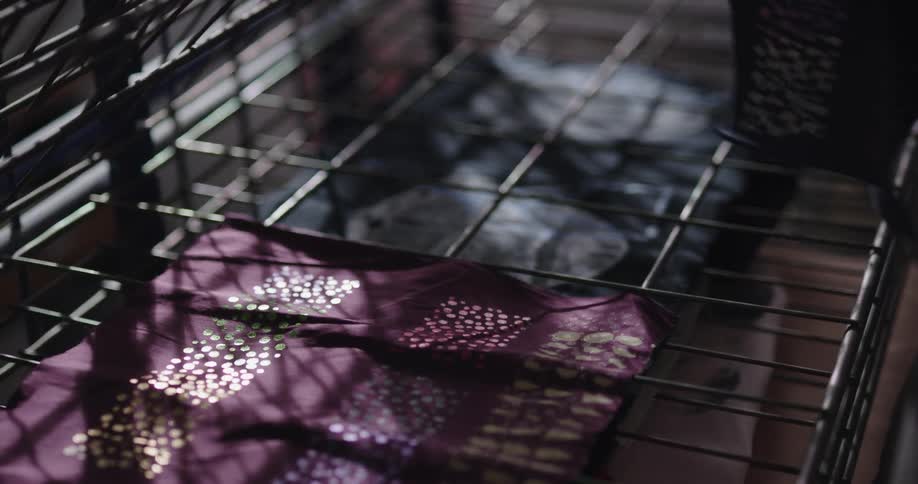 Person lays paint decorated fabric on folding metal racks