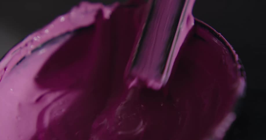 A stick mixing pink paint in a container on a table