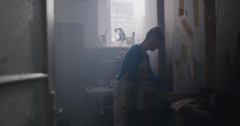Woman in an apron puts on gloves then uses a hose to clean a sink