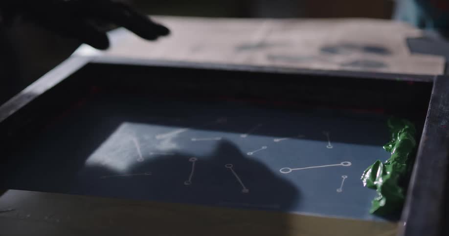 Two people are putting ink in a silk screener and scraping it on the fabric