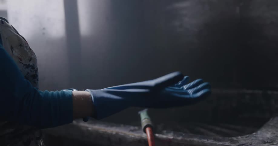 A woman puts on gloves and sprays water in to a large sink as she holds a small object