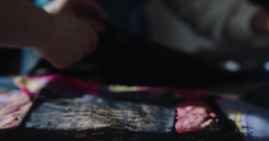 Two people are moving quilts around on a table