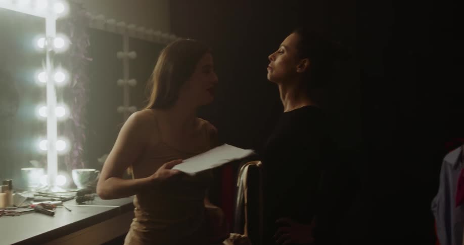 Two women in a dressing room arguing with a wall and mirror in the background
