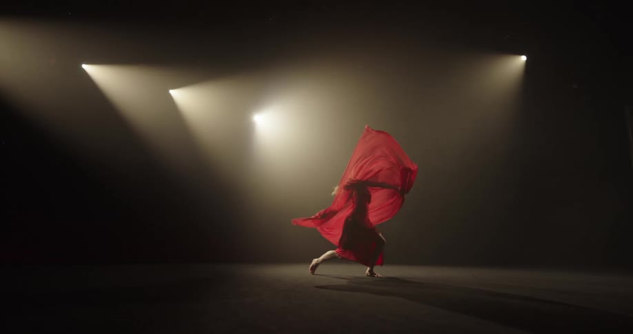 A dancer in a red dress moves on stage while waving a large red scarf around