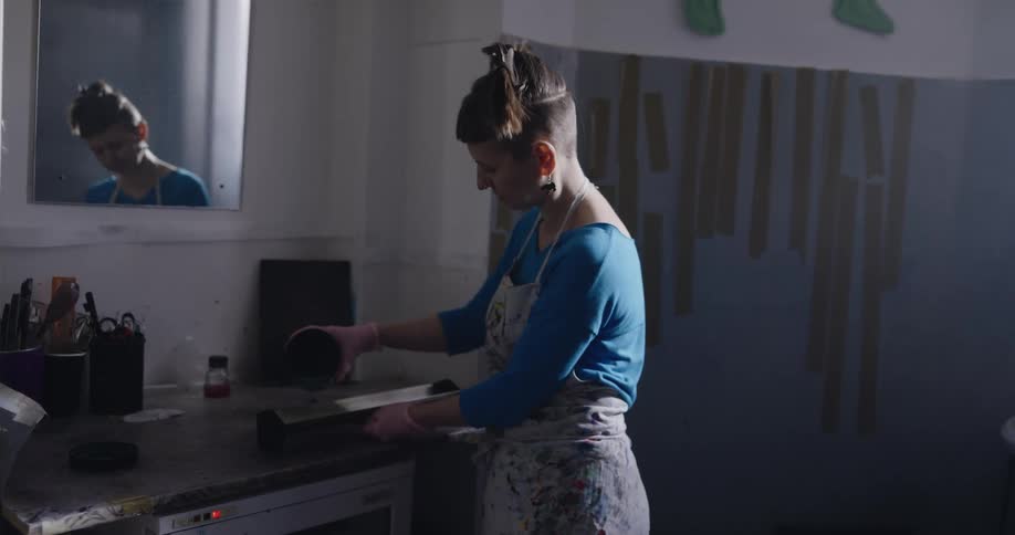 A woman wearing an apron is pouring paint into a container