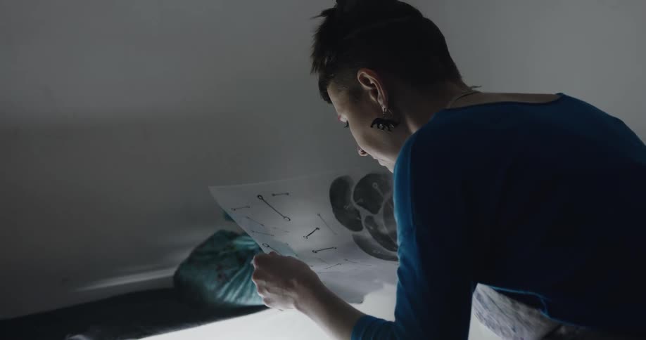 A woman in a room looking at a plastic slide with a wall and a plastic bag in the background