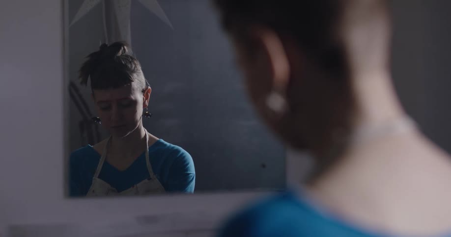 A woman with an apron in a room with a wall and mirror in the background