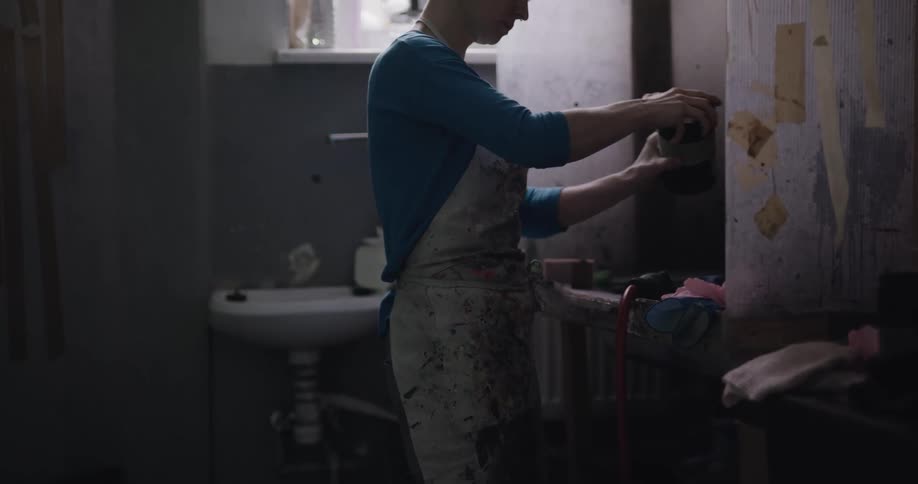 A woman with an apron in a room closing a jar and picking up a glove